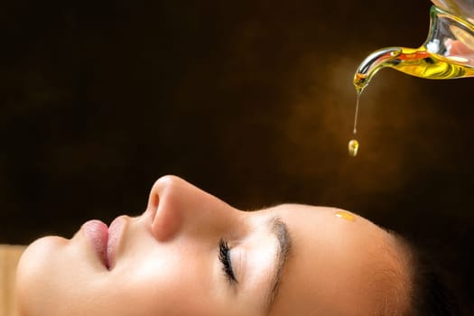 Macro close up portrait of young woman at ayurvedic massage session with aromatic oil dripping on face.