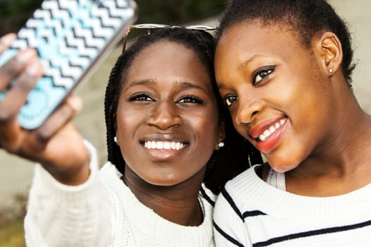 Close up face shot of two afro american teen girls taking self portrait with smart phone.