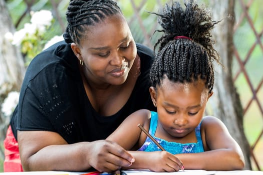 Close up portrait of african teacher supervising little kid doing homework outdoors.