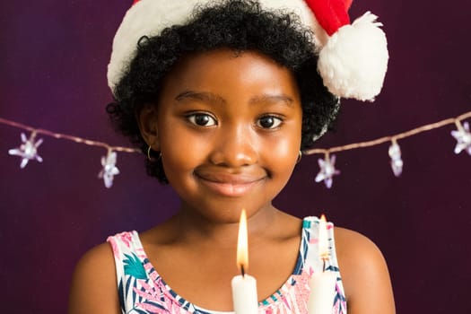 Close up face shot of little afro american girl with christmas hat holding candles.