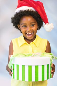 Close up portrait of happy african kid holding christmas gift boxes.Girl wearing red hat against light blue background.