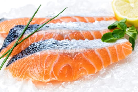 Macro close up of fresh salmon filets layed on crushed ice with lemon and greens in background.