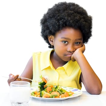 Close up portrait of little african girl sitting in front of healthy vegetable dish.Long faced kid with afro hairstyle Isolated on white background.