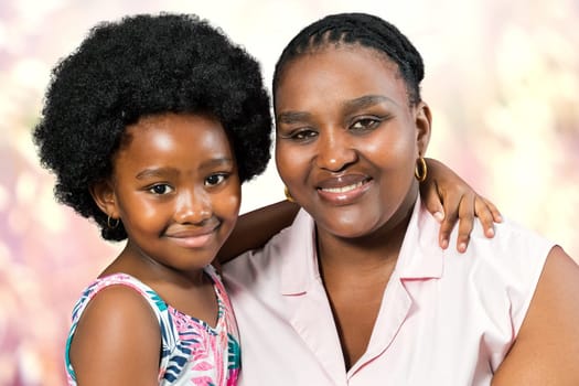 Close up studio portrait of little african girl embracing mom against colorful background.