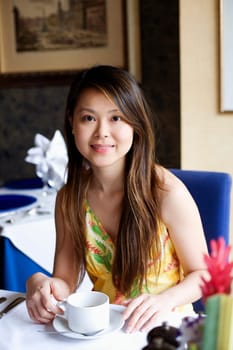 Portrait of a young woman sitting in a restaurant holding a cup of coffee