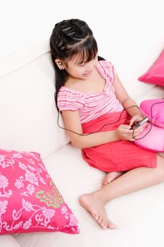 High angle view of a girl sitting on a couch and listening to an MP3 player