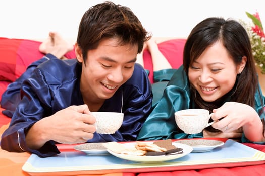Close-up of a mid adult man holding a cup and lying on the bed with a young woman