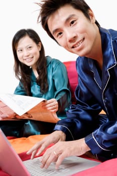 Portrait of a mid adult man using a laptop and young woman reading a newspaper