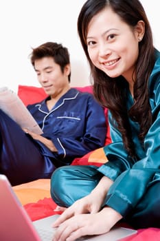 Portrait of a young woman using a laptop and mid adult man reading a newspaper