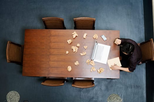 High angle view of a businessman writing on a notepad with crushed papers on the table