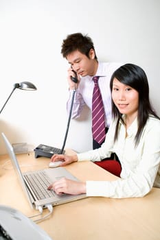 Businesswoman using a laptop with a businessman talking on the telephone