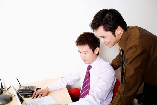 Side profile of a businessman using a laptop with another businessman standing behind him