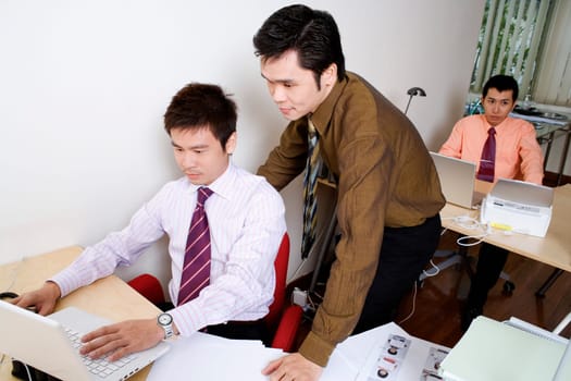 Businessman using a laptop with another businessman standing behind him