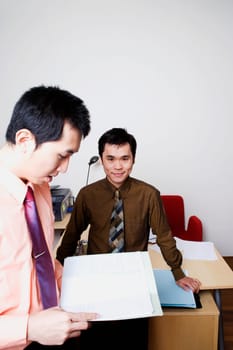 Portrait of a businessman smiling with another businessman reading a file
