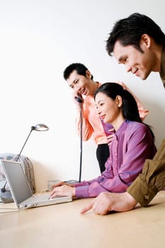 Side profile of a businesswoman using a laptop with two businessmen standing beside her