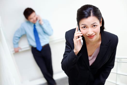 Portrait of a businesswoman talking on a mobile phone with a businessman standing behind her