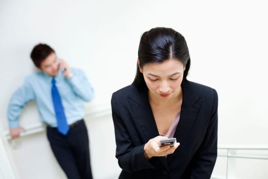 Businesswoman operating a mobile phone with a businessman standing behind her