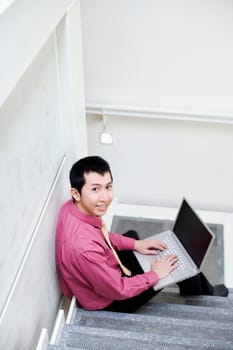 Portrait of a businessman sitting on steps and using a laptop