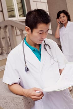 Close-up of a male doctor reading a report with a female doctor talking on mobile phone in the background