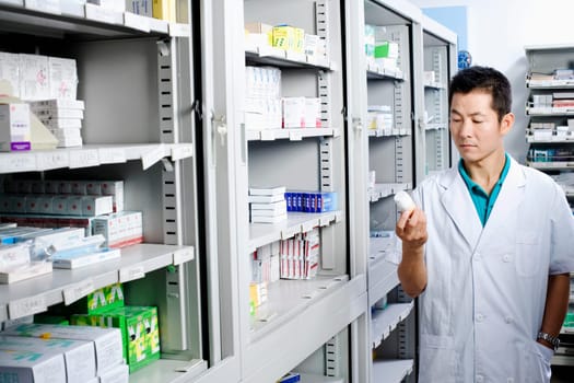 Male pharmacist looking at a bottle in a store room