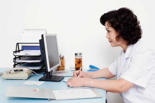 Close-up of a female doctor looking at a computer monitor and writing on a notepad