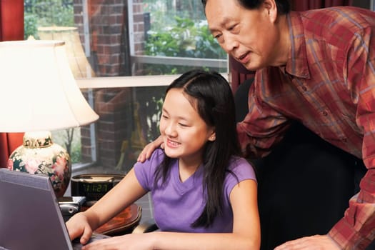Close-up of a girl using a laptop with her father behind her