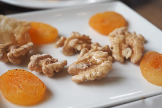 Dried apricots and walnuts are arranged attractively on a plate.