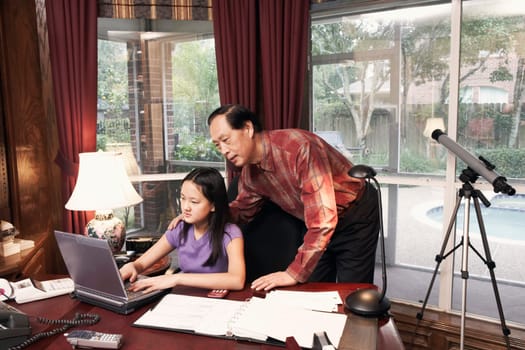 Girl using a laptop with her grandfather standing beside her