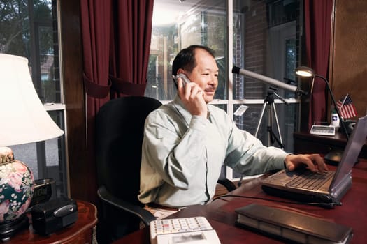 Senior man using a laptop talking on a cordless telephone