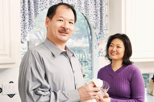Portrait of a senior man cleaning a glass with a mature woman standing behind him