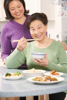 Portrait of a senior woman eating food with her daughter standing behind her