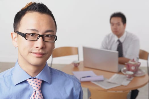 Portrait of a businessman smiling with another businessman using a laptop behind him