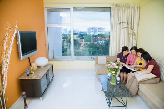 Three senior women and a mature woman sitting on a couch and looking at a photo album