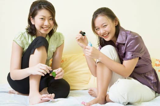 Portrait of two young women applying nail polish on their toenails
