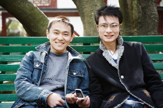 Portrait of a young man sitting together with his friend holding a mobile phone