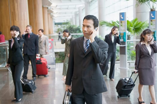 Business executives talking on mobile phones and leaving an airport lounge