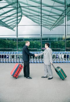 Side profile of two businessmen shaking hands outside an airport