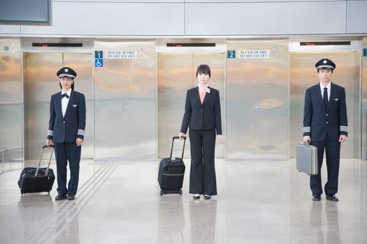Male and a female pilot standing with a female cabin crew in front of elevators