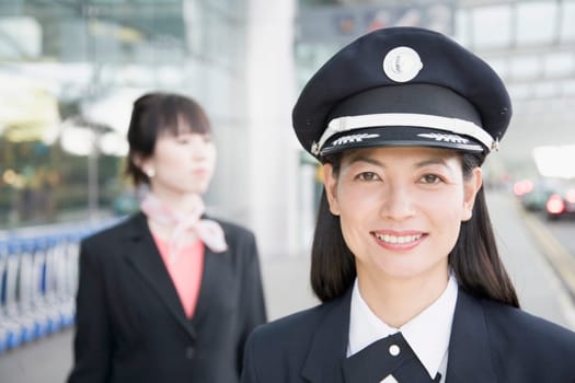 Close-up of a female pilot smiling with a female cabin crew behind her