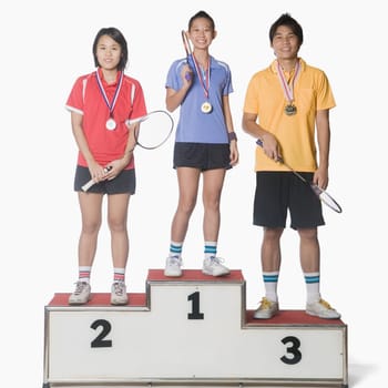 Portrait of two young women and a young man standing on a winners podium and wearing sports medal
