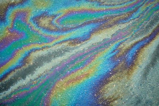Vivid patterns created by an oil slick on the asphalt underscore the effects of rain in urban landscapes, raising awareness about the challenges of environmental pollution