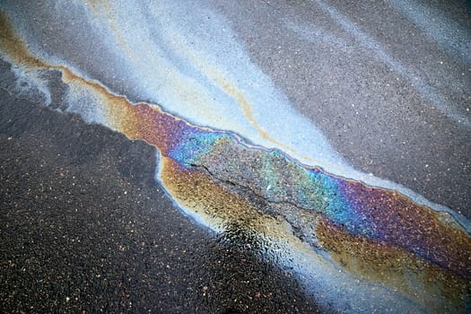 A brightly colored gasoline or oil spill creates a colorful sheen on a cracked asphalt surface
