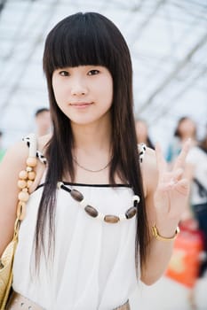 Portrait of a young woman standing in a corridor and making a peace sign