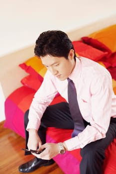High angle view of a businessman sitting on the bed and operating a mobile phone