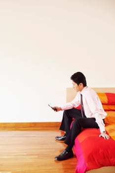 Side profile of a businessman sitting on the bed and operating a mobile phone