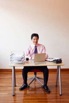 Portrait of a businessman sitting in an office with a laptop and smiling