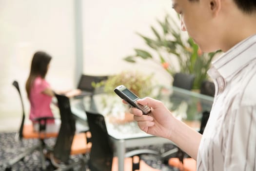 Side profile of a male office worker operating a mobile phone in an office
