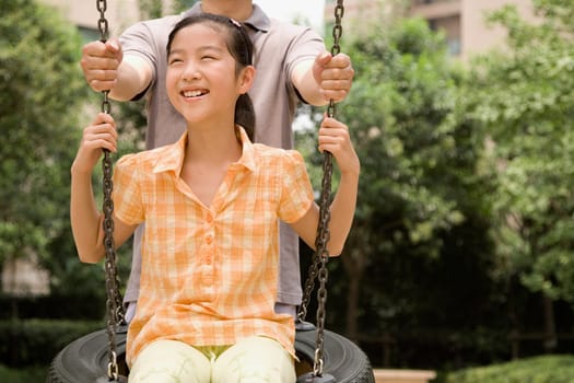 Girl swinging on a tire swing with her father standing behind her