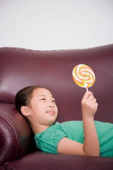 Side profile of a girl lying on a couch and holding a lollipop
