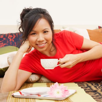 Portrait of a young woman lying on the bed and holding a cup of tea